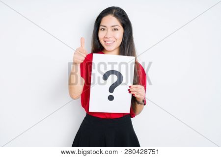 Young brunette woman holding paper with question mark over isolated background happy with big smile doing ok sign, thumb up with fingers, excellent sign