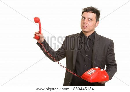 Studio Shot Of Caucasian Businessman Looking Annoyed While Holdi