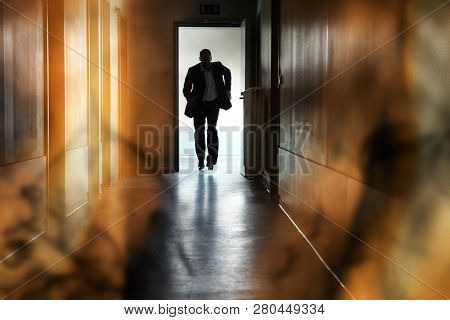 Silhouette Of Person Running Out Of Fire Escape On Corridor Of Building