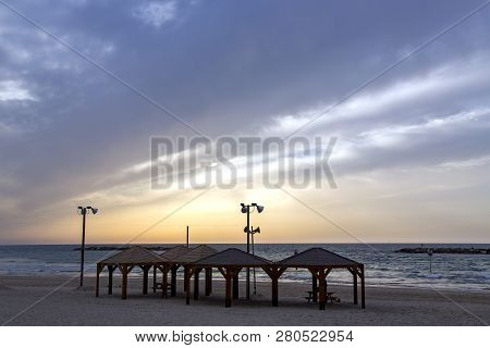 View Of Beach With Wooden Arbors Against Sunset Of Mediterranean Sea In Tel Aviv, Israel