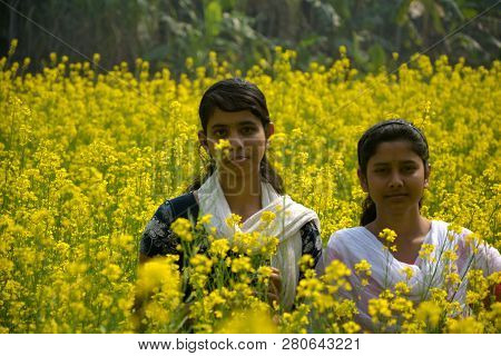 Two Beautiful Asian Teens Standing In A Mustard, Rape Field With Yellow Color Flowers, Covering Head