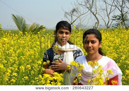 Two Beautiful Asian Teens Standing In A Mustard, Rape Field With Yellow Color Flowers, Covering Head