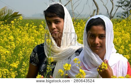 Two Beautiful Asian Teens Standing In A Mustard, Rape Field With Yellow Color Flowers, Covering Head