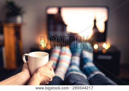 Couple Drinking Tea, Hot Chocolate, Eggnog Or Mulled Wine And Watching Tv In Warm Cozy Woolen Socks 