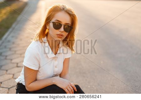 Portrait Of A Beautiful Hipster Young Woman In Stylish Sunglasses In A White Polo T-shirt In Black J