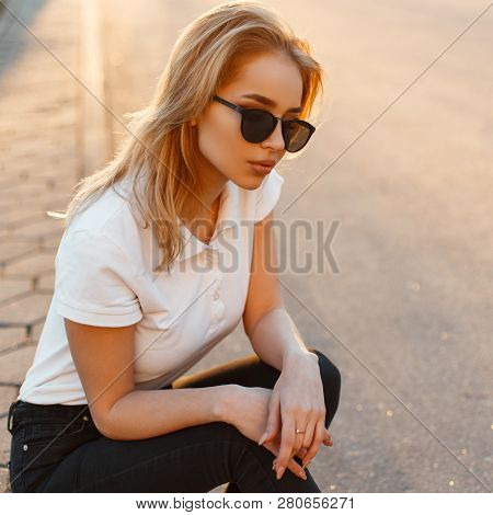 Portrait Of A Beautiful Hipster Young Woman In Stylish Sunglasses In A White Polo T-shirt In Black J