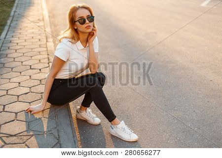 Young Woman Hipster In Stylish Sunglasses In A White Polo Shirt In Black Jeans In White Fashionable