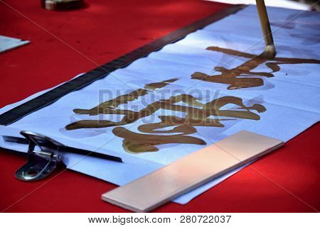 A Hand Holding A Paintbrush Is Writing With Golden Ink Spring Couplet. Translation Of Character Is  