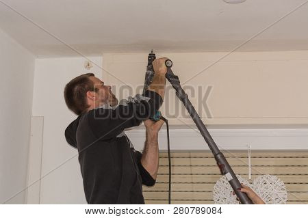 The Man Drills A Hole In The Ceiling Before Mounting A Curtain Rod