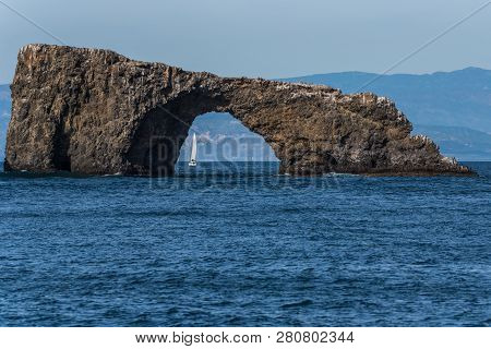 Small Sailboat Is Visible Through The Anacapa Island Arch On A Sunny Winter Day In The Channel Islan