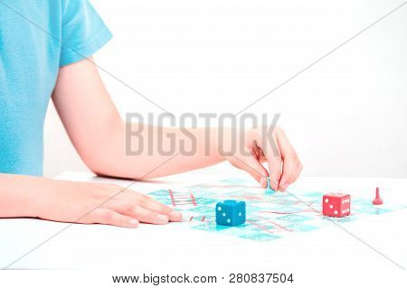 Child Plays A Board Game Snakes And Ladders With Colorful Pieces And Dice With Both Hands On Tableto
