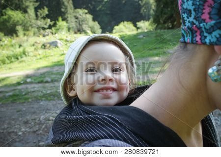 Mother Carrying A Two Year Old Smiling Baby In A Black Woven Wrap. Tracking, Outdoor