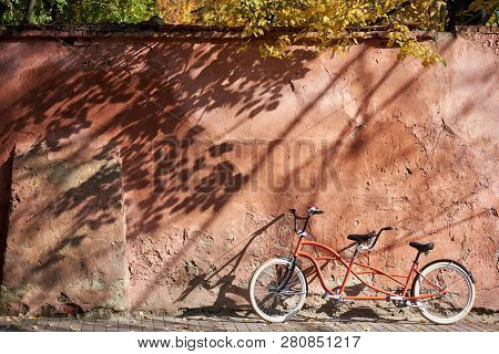 Modern Comfortable Orange Tandem Double Bicycle With White Wheels On Paved Empty Sidewalk Leaned Aga