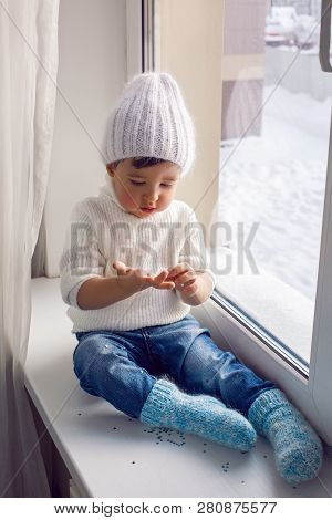 Boy In A White Sweater Standing At The Window On The Windowsill