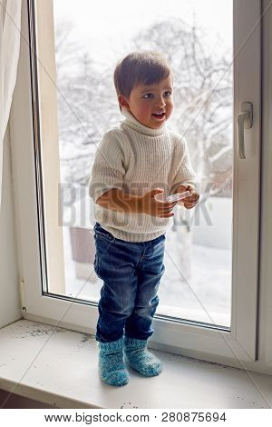 Boy In A White Sweater Standing At The Window On The Windowsill
