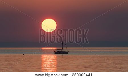 Sunset With Sailing Boat And Some Rocks In The Foreground In Cres