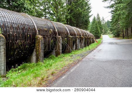 Water Sprays Out Of A Wooden Water Flume That Is Supported On Concrete Wedges Next To The Parking Ar