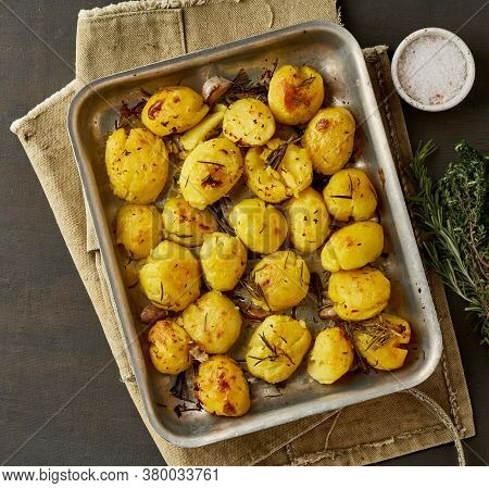Oven Baked Whole Crushed And Crusty Potato Spuds With Seasoning And Herbs In Metalic Tray.