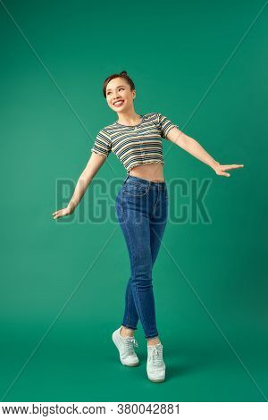 Joyful Young Asian Woman Standing On One Leg. Full Length View Of Blissful Girl Dancing On Green Bac