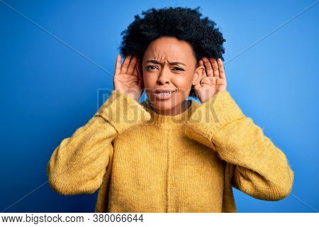 Young beautiful African American afro woman with curly hair wearing yellow casual sweater Trying to hear both hands on ear gesture, curious for gossip. Hearing problem, deaf