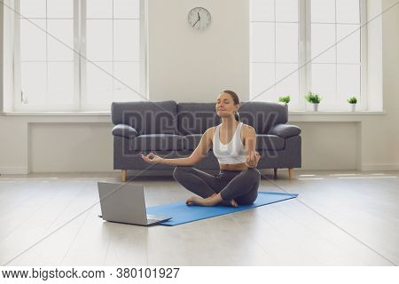 Online Yoga Maditation Home.attractive Young Girl Sitting In Lotus Pose Near Laptop At Home. Fit Wom