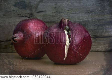 Two Entire (whole) Pomegranate Fruits On Wood Table Against Wooden Background With Grunge Filter App