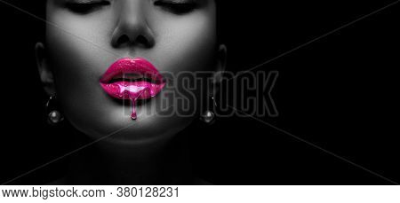 Purple Paint dripping, lipgloss drops on sexy lips, bright liquid paint on beautiful model girl's mouth, black skin. Lipstick. Make-up. Beauty face makeup, close up. Isolated on black background