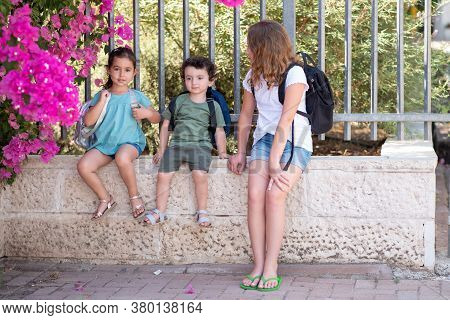 A Young Sisters And Brother Wait Outisde A Closed School Gate.