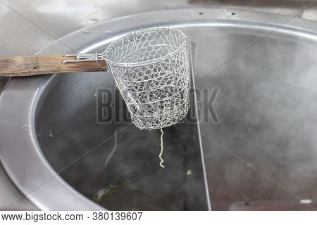 Strainer Basket For Blanching Noodles Laying Over A Pot Covered With Steam.