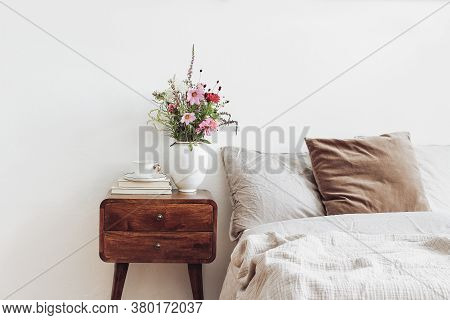 Cup Of Coffee And Books On Retro Wooden Bedside Table. Rustic White Ceramic Vase With Bouquet Of Pin