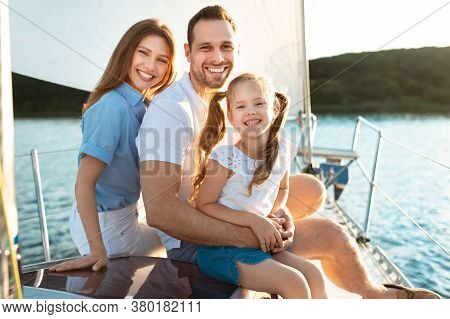 Family Of Three Relaxing On Yacht Hugging Smiling To Camera Sitting On Boat Deck Outdoors. Dream Vac