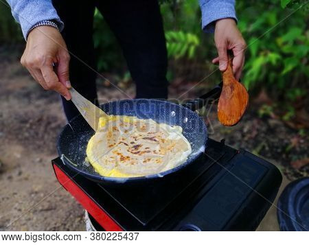 Asian Woman Cooking Roti Canai At Forest During Outdoor Camping.