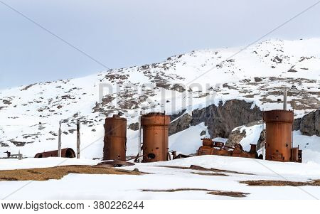 Abandoned marble mining machinery at Camp Mansfield, New London, Svalbard. Snow covered mountain background with blue sky.
