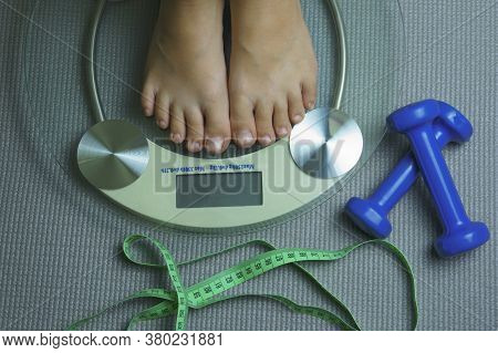 Two Blue Dumbbells, Legs On A Scale And A Ruler On A Yoga Mat In The Gym. Sports, Fitness, Weightlif