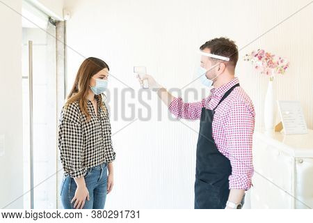 Male Hairdresser Checking Temperature Of Female Client Through Thermal Scanner At Beauty Studio