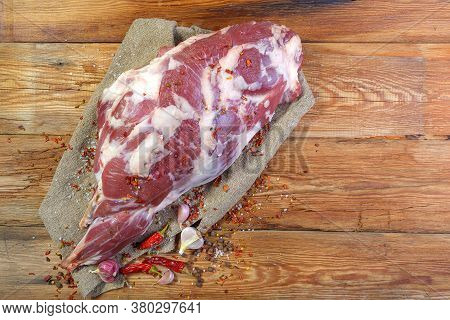 On A Wooden Table Lies A Raw Leg Of Mutton On A Bone. Sheep Meat Close-up.a Fresh Piece Of Mutton. T