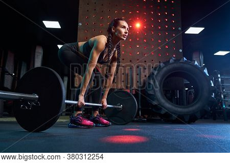 Side View Of Brunette Female Bodybuilder With Long Braids Doing Deadlift Using Barbell. Srtong Woman