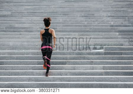 Muscular African American Girl In Sportswear Runs Up The Stairs In City At Summer, Back, Free Space