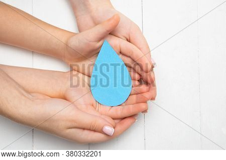 Human Hands Holding Water Drop Isolated On White Wooden Background. Top View. Eco Friendly Living, H