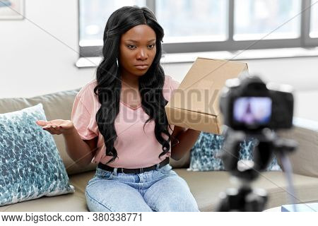 blogging, videoblog and people concept - african american female video blogger with parcel box and camera videoblogging at home