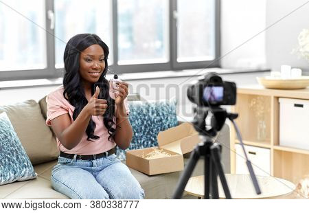 blogging, videoblog and people concept - happy smiling african american female beauty blogger with camera and perfume videoblogging at home