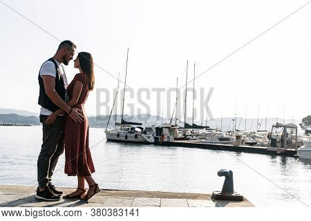 Beautiful Couple In Love On The Seashore. They Are Standing Face To Face, Yachts And Sailboats In Th