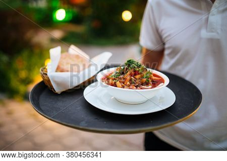Waiter Holding Round Tray With Uyghur Dish Guiru Lagman And Bread With A Blurry Background