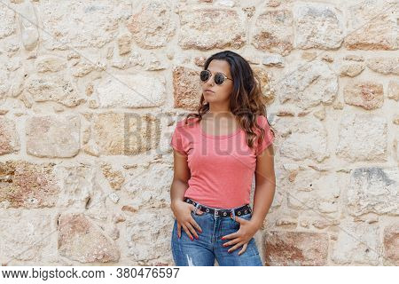 Young Women Wearing T-shirt And Jeans Stays Near A Wall And Smile