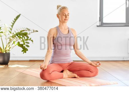 mindfulness, spirituality and yoga concept - happy young woman meditating in lotus pose at home