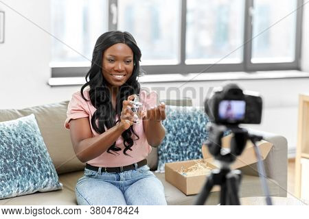 blogging, videoblog and people concept - happy smiling african american female beauty blogger with camera and perfume videoblogging at home