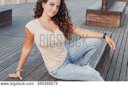 Young Women Wearing T-shirt And Jeans Sits On The Wooden  Bench