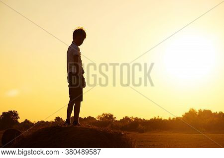 Silhouette Of A Child-boy Standing On A Haystack Against The Background Of A Field With A Beautiful 