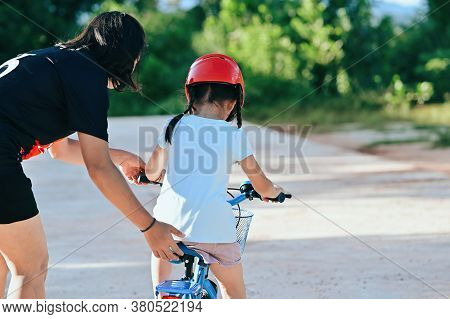 Happy Mother Teaching Little Daughter To Ride A Bicycle. Child Learning To Ride A Bike In The Park A