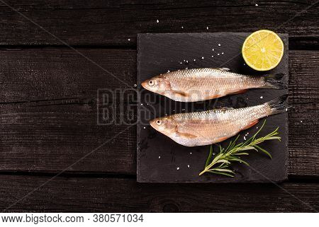 Raw Fish With Lime And Rosmary On Black Wooden Plank. Top View With Copy Space.